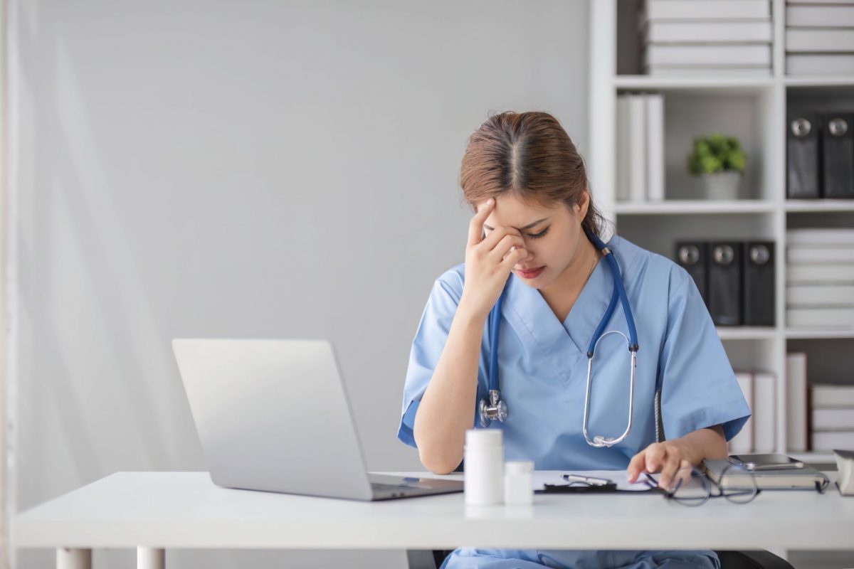 Stressed young female doctor looking at laptop reading bad news online worried of mistake at workplace. Unhappy professional physician in tension feeling tired solving computer problem at work.